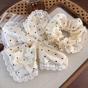 Détail d'un chouchou à pois crème avec bordure en dentelle et nœud sur plateau en bois