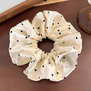 Détail du chouchou en satin à pois beige sur bois avec une finition de texture soyeuse