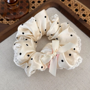 Détail d'un chouchou à pois avec bordure en dentelle et nœud en soie sur lin