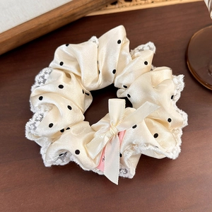 Détail d'un chouchou en satin crème à pois avec bordure en dentelle et nœud