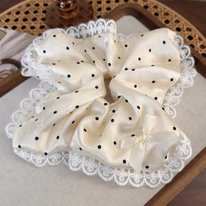 Détail d'un chouchou à pois blanc crème avec bordure en dentelle et nœud en soie
