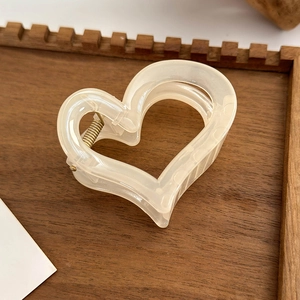 Detailed macro view of heart-shaped cream translucent hair claw clip with golden metal spring