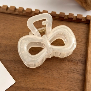 Detail of cream white resin claw clip with elegant bow design and sturdy metal spring
