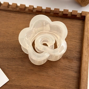 Detail shot of a translucent cream camellia hair claw clip on a decorative wooden tray