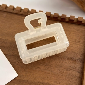Detail of a creamy white rectangular resin hair claw clip displayed on a wooden tray