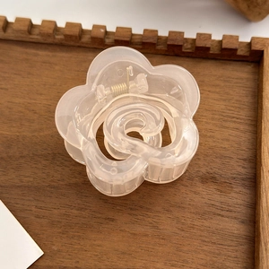 Detail of peach resin camellia hair claw clip with golden spring on dark wood tray