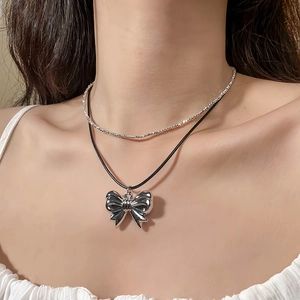 Detailed view of a double-layered necklace featuring a large metallic silver bow pendant