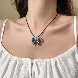 Elegant silver metal bow pendant with black cord chain worn by a female model