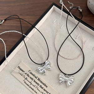 Silver bow necklace with beaded chains and black leather cord in a jewelry box