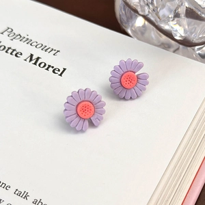 Dettaglio degli orecchini a forma di margherita viola su sfondo di carta bianca decorata