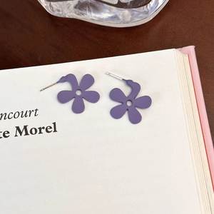Orecchini a perno a fiore viola opaco su uno sfondo di libro dallo stile minimalista