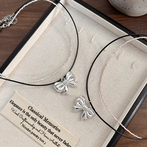 Detail of elegant silver bow pendants on thin black cord and beaded necklaces