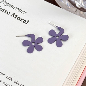Dettaglio di orecchini a lobo a fiore viola con finitura opaca su pagine di un libro