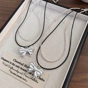 Detailed close-up of double-layer bow necklaces with shiny metal beads on a wood tray