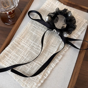 Elegant black mesh scrunchie with white pearls and long satin ribbons on linen surface