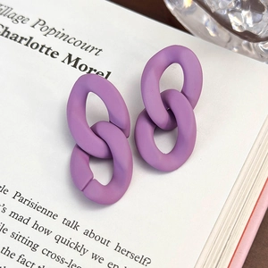 Dettaglio di orecchini a doppia maglia viola opaco posati su un libro in luce soffusa
