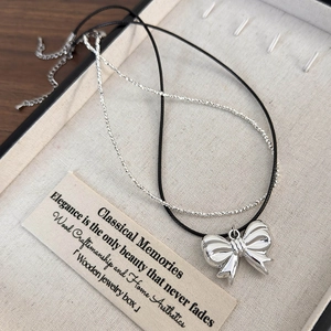 Detail of a double-layered necklace with a polished silver bow pendant in a gift box