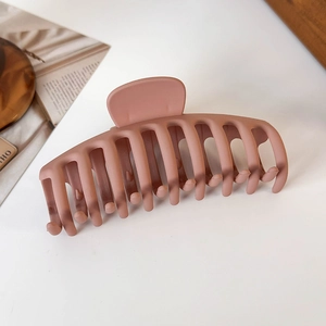Detail view of large matte pink hair claw clip with multi-tooth structure on white surface
