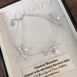 Vue détaillée du collier à nœud argenté avec perles dans un coffret à bijoux de qualité