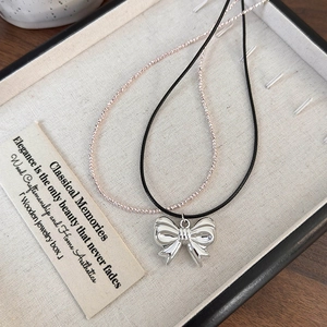 Detail of silver bow pendant necklace with shiny metallic finish and double layered chain