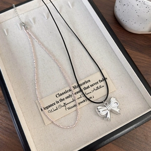 Detail of silver bow pendant on black cord and dainty beaded necklace in a jewelry tray