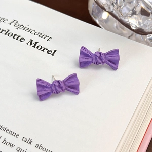 Dettaglio macro di orecchini a fiocco viola con superficie testurizzata su bianco