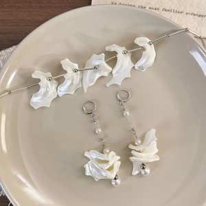 Macro detail of seashell necklace and pearl earrings set on a beige ceramic plate