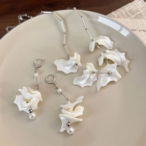 Macro detail of iridescent shell petal necklace and pearl earrings on ceramic tray