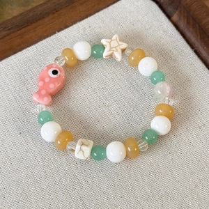 Dettaglio di bracciale con perline colorate, ciondolo a forma di pesce rosa e stella su fondo