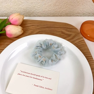 Détail d'un chouchou en maille bleu clair à motif marguerites sur plateau blanc