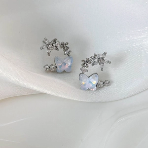 Macro shot of silver petal butterfly earrings with zircon stones on silk fabric