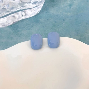 Primo piano di orecchini rettangolari in resina azzurra su un piatto di ceramica bianca