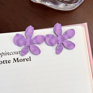 Dettaglio di orecchini a fiore viola opaco su un libro, mostrando la trama dei petali