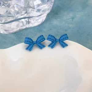 Dettaglio di orecchini a fiocco blu reale con trama cucita su piatto bianco