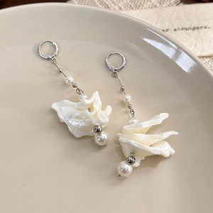 Detail of elegant shell and pearl drop earrings displayed on a beige ceramic plate