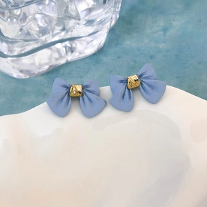 Dettaglio orecchini a fiocco blu opaco con centro dorato su un vassoio bianco elegante