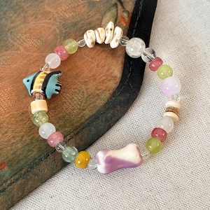 Dettaglio di bracciale con perline con ciondoli a pesce e osso su tessuto vintage