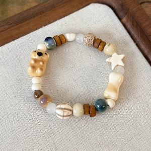 Dettaglio di bracciale con perline, orsetto in ceramica, stella e ciondoli a forma di osso