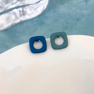 Dettaglio di orecchini quadrati geometrici blu opaco con design cavo su bordo ceramico