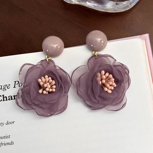 Dettaglio di orecchini a fiore in tulle viola con perni lavanda su una pagina di libro