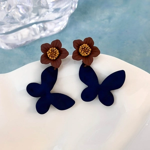 Dettaglio macro di orecchini pendenti con fiori e farfalle blu opaco su un piatto bianco