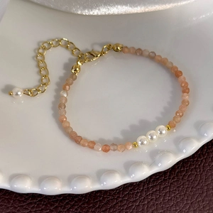 Detail of sunstone beaded bracelet with white pearls and gold metal spacers on ceramic tray