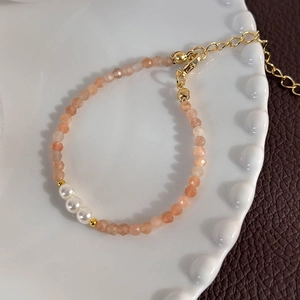 Detailed macro view of orange-pink faceted crystal beads and white pearls on the bracelet