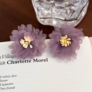 Dettaglio ravvicinato di orecchini a fiore in tulle viola su un libro bianco
