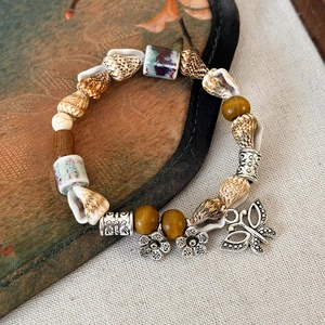 Dettaglio di bracciale boho con perline in ceramica, conchiglie e farfalla