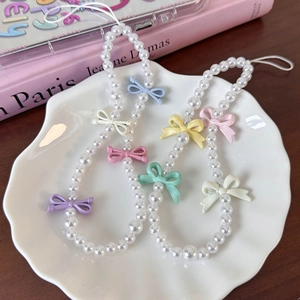 Close-up of colorful bow charms and white pearls on phone lanyards in a shell tray