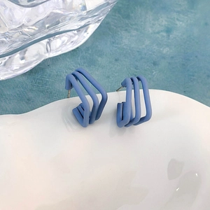 Dettaglio di orecchini geometrici blu opaco presentati su un piatto di ceramica bianca