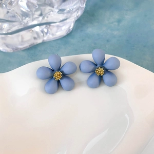 Macro di orecchini a fiore blu opaco con stami dorati su un piatto di porcellana bianca