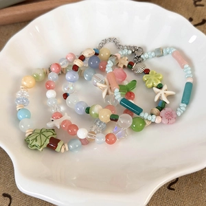 Detail of colorful beaded bracelets with starfish and shell charms in a shell dish