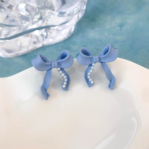 Dettaglio di orecchini a fiocco azzurro con mini perle bianche su un piatto bianco